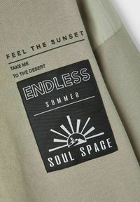 Light olive green fabric features a black patch with white text and graphic sun design. Phrases include "ENDLESS SUMMER" and "SOUL SPACE."