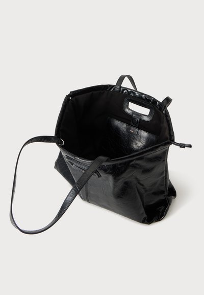 Sac cabas en cuir noir avec longue bandoulière et grande poche intérieure à fermeture par bouton, présenté ouvert sur fond blanc.