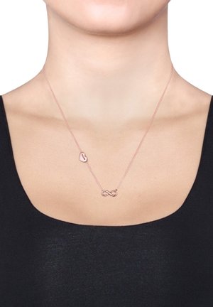Rose gold halskæde med en fin kæde, der har en lille hjertecharm og et uendelighedssymbol, vist mod en mørk top.