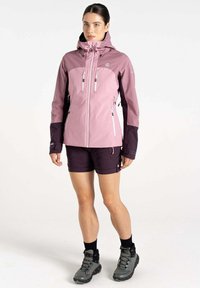 Rosa und lila wasserdichte Jacke mit Kapuze, ausgestattet mit zwei Reißverschluss-Brusttaschen und elastischen Bündchen, getragen mit dunklen Shorts und Wanderstiefeln.