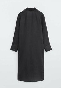 Long manteau noir à manches longues, larges poignets et col classique présenté de dos sur un fond clair uni.