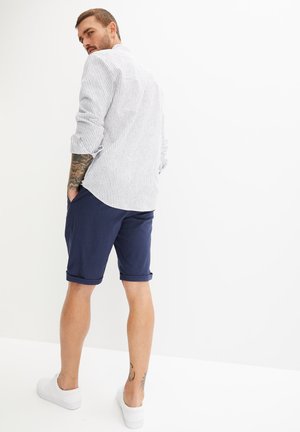 Outfit da uomo caratterizzato da una camicia a righe a maniche lunghe bianca e blu navy, abbinata a pantaloni corti blu navy e scarpe bianche, che mette in risalto un design casual.