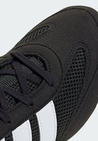 Czarne buty sportowe z siateczkową cholewką, wyściełanym kołnierzem i białymi paskami. Sznurowadła są wyraźnie przeplatane przez oczka, co zapewnia pewne dopasowanie.