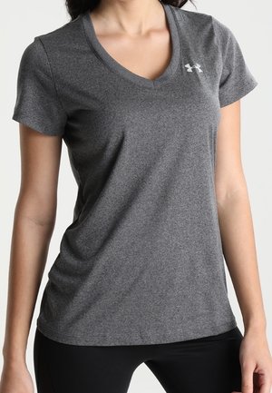 Femme portant un t-shirt de sport ajusté à manches courtes gris foncé avec un petit logo blanc sur le haut de la poitrine.