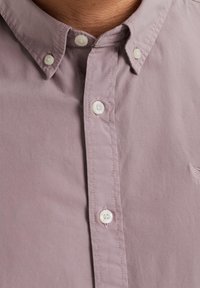 Camicia button-up di un leggero viola con una morbida texture, caratterizzata da bottoni bianchi, colletto e delicate cuciture decorative lungo la patta.