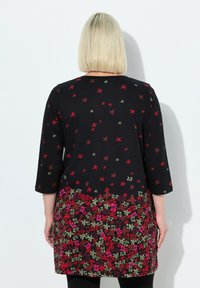 Zwarte tuniekjurk met driekwartmouwen. Bloemenpatroon in rood, groen en roze op de onderste helft. Zachte, geweven stof.