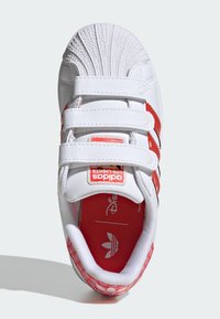 Biele tenisky s červenými akcentmi, ktoré majú textúrovaný špic, suché zipsy a vzorovanú podrážku s kresleným dizajnom.