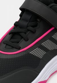 Juodas sportinis batelis su rožinėmis detalėmis, juodais raišteliais, velcro dirželiu ir baltu padu, kuris turi atspindinčias sidabrines juosteles.