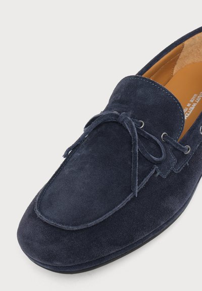Mocassin en daim bleu marine avec un détail de laçage en nœud, bout rond et doublure intérieure en cuir fauve.