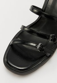 Black leather open-toe sandal featuring three thin straps and adjustable buckles, with a smooth texture and a low, square-shaped heel.