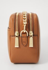 Tan leren tas met een gestructureerde afwerking, voorzien van twee gouden ritsen en kettinghardware, compact rechthoekig ontwerp en gouden accenten.