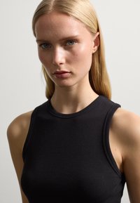 Schwarzes geripptes Tanktop mit hohem Ausschnitt und ärmellosem Design, das eine figurbetonte Silhouette und eine glatte Textur aufweist.