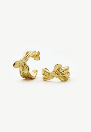 Pendientes de metal tono dorado con forma de cintas retorcidas atadas en nudos, con superficies lisas y pulidas y estilo de aro.