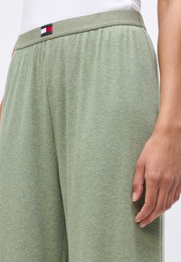 Kadar u krupnom planu osobe koja nosi svijetlozelene rebraste pletene hlače s elastičnom waistbandom i malim Tommy Hilfiger logo zakrpom.