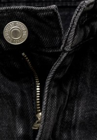 Black denim jacket interior with a silver metal snap button and zipper. Features gray fabric texture and stitching detail along the edges.