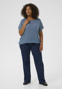 Helles blaues Kurzarmtop mit lässiger Passform, kombiniert mit dunkelblauen geraden Jeans. Der Stoff wirkt weich und hat eine glatte Textur.