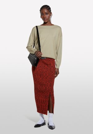 Maglietta beige chiaro a maniche lunghe, gonna rossa a fantasia aderente con spacco, borsa nera a spalla, calzini bianchi e ballerine nere. Design minimalista.