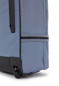 Maleta de viaje de tela azul con superficie texturizada, base de goma negra, asa retráctil y dos ruedas para mayor movilidad.