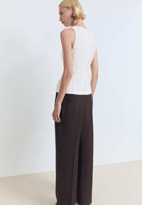 Sleeveless cream top with a fitted design, featuring vertical seams; paired with loose, dark brown wide-leg trousers.