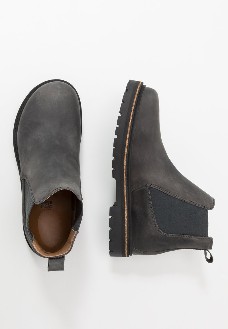 Stivali alla caviglia in pelle nera con pannelli elasticizzati laterali, finitura texturizzata e suola in gomma robusta caratterizzata da una striscia marrone a contrasto.