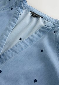 Šviesiai mėlyna džinsinė palaidinė su V formos iškirpte, ant audinio tolygiai išdėstyti mažyčiai tamsiai mėlyni širdelių raštai. Pagaminta iš minkšto medvilnės mišinio.