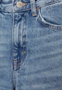 Vaaleansiniset farkut, joissa on korkea vyötärö, etutaskut ja kuparinvärinen ommel. Farkuissa on napitus ja lievää kulutusta.