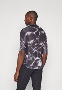 T-shirt de sport à manches courtes en noir avec un motif aquatique. Fabriqué en matériau lisse et extensible avec un design ajusté et un détail de poche à l'arrière.