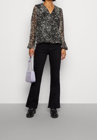 Czarna kwiatowa bluzka kopertowa z przezroczystymi długimi rękawami, w zestawieniu z czarnymi dzwonami i małą, teksturowaną torebką w odcieniu lawendy. Czarne masywne buty.