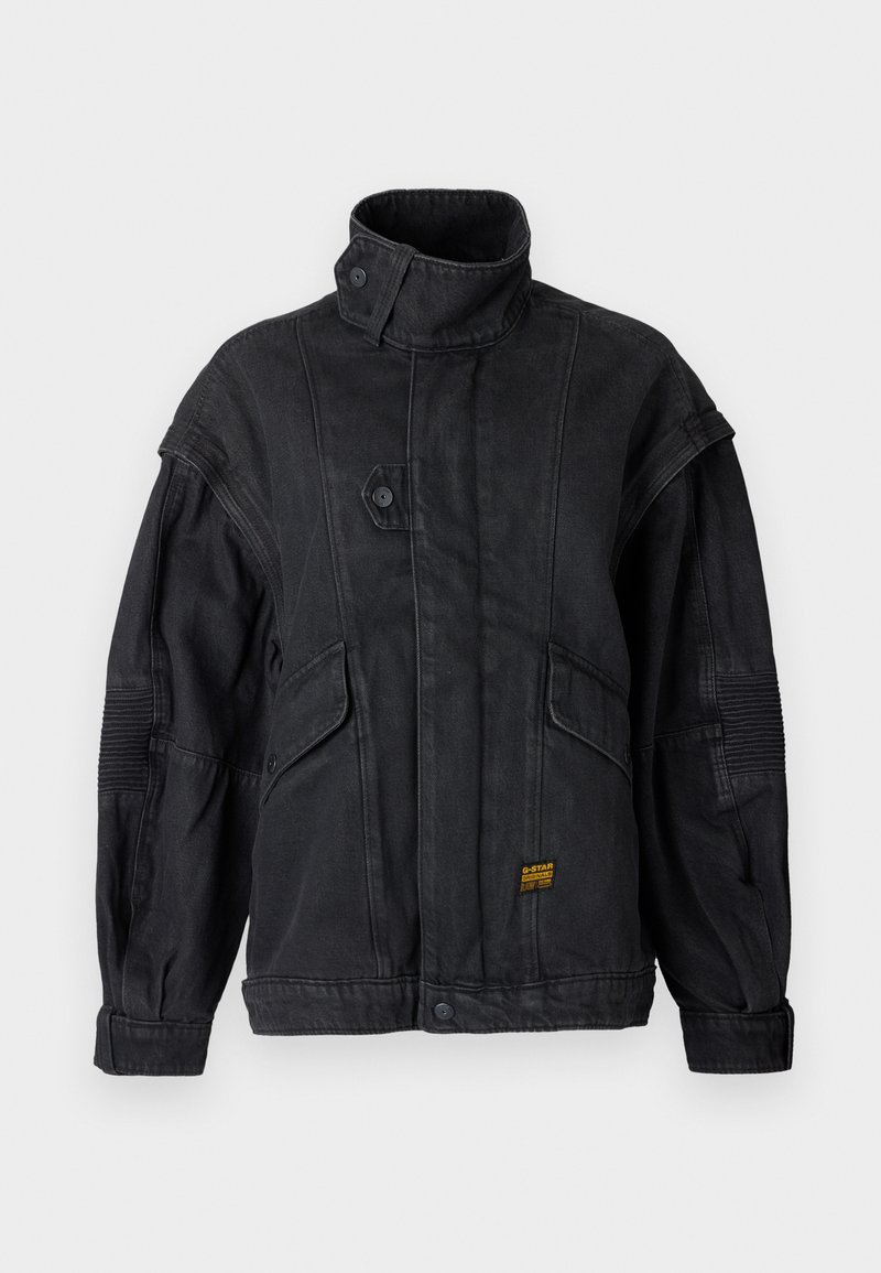 Veste noire à col haut avec fermeture à boutons, poches à rabat, détail de coude cousu et petite étiquette de marque jaune en bas sur le devant.