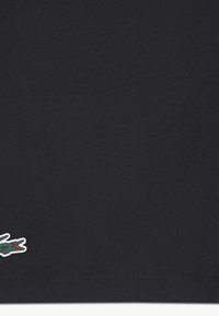 Sort polotrøye laget av teksturert stoff, med en liten farget krokodillelogo nederst til venstre.