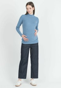 Top a maniche lunghe di colore azzurro chiaro con righe e scollo alto, abbinato a jeans a gamba larga di colore scuro e sneaker bianche con dettagli beige.
