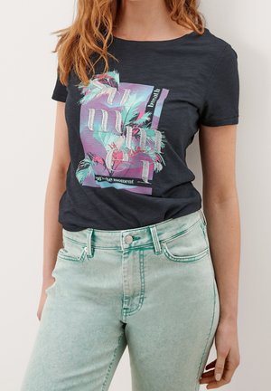 Schwarzes Baumwoll-T-Shirt mit einem farbenfrohen Grafikdruck mit Palmblättern und dem Wort "Sommer". Kombiniert mit hellgrünen Jeans aus Denim.