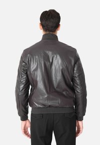 Giubbotto bomber in pelle marrone con colletto e polsini a coste, caratterizzato da una superficie liscia e leggermente lucida e una silhouette aderente.