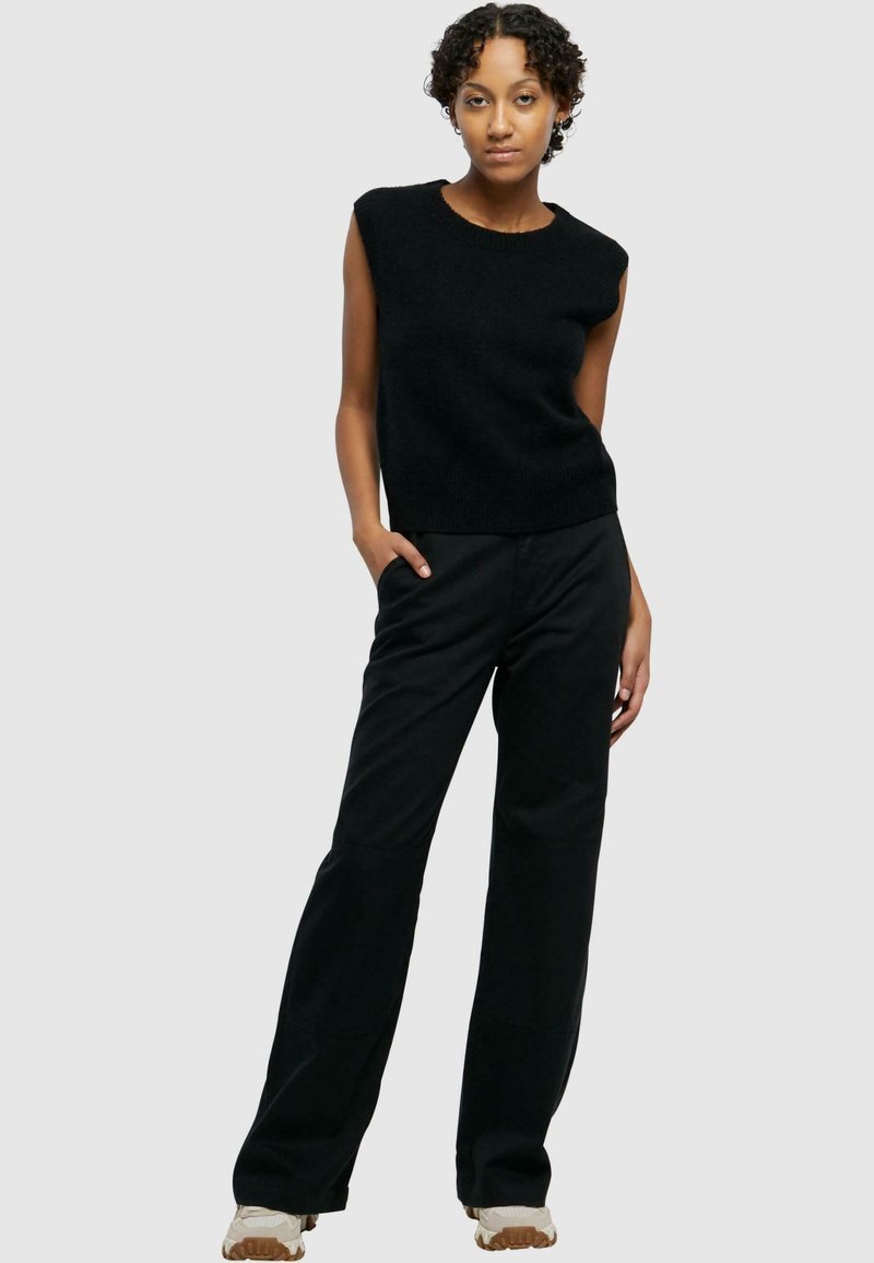 Zwarte mouwloze gebreide top met een ronde halslijn, gecombineerd met hoge zwarte broek en lichtgekleurde sneakers. Glad textuur, casual fit.