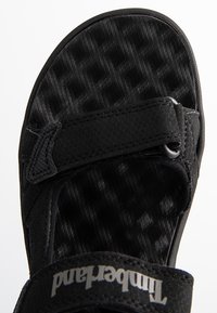 Sandalia negra con plantilla texturizada y correa ajustable de Velcro. Diseño ligero, con suela de goma para mayor tracción.