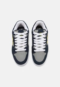 Navy and grey sneakers featuring white laces, perforated toe box, and yellow accent stripes. Textured upper material and cushioned sole.