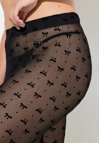 Černé průhledné punčocháče s opakujícím se vzorem mašlí a puntíků. Pas je v pevné černé barvě s hladkou texturou.