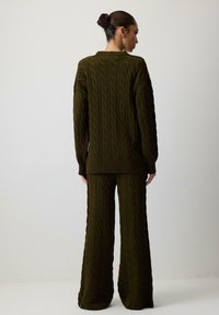 Žalias megztinis ir plačios kojinės kelnės, pasižyminčios tekstūruotu kabelių raštu. Laisvas siluetas su aplinkais ir apatinėmis dalimis su pūkeliu.