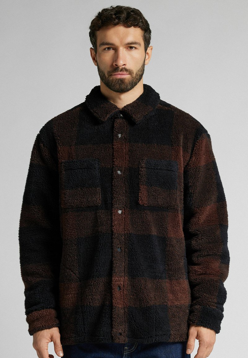 Brun och svart rutig fleecejacka med krage, två bröstfickor och knäppning; mjuk textur; avslappnad passform.