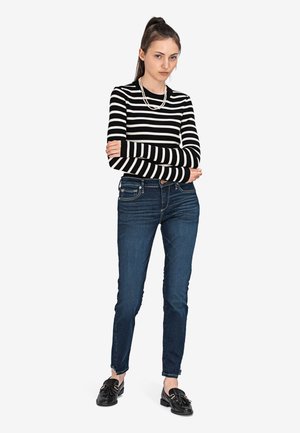 Zwart-wit gestreepte langslijftop, strakke donkerblauwe jeans en zwarte instapper. Eenvoudig ontwerp met geribbelde textuur en parelketting.