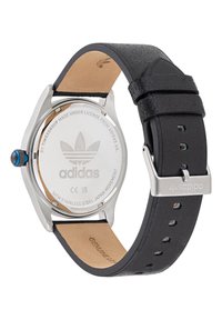 Nerūsējošā tērauda pulkstenis ar apaļu seju, melnu ādas siksnu un zilu kroni. Iegravēts Adidas logo aizmugurē, strukturēta siksnas detaļa.