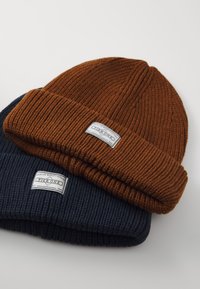Two ribbed knit beanies: one in dark navy blue and one in brown, both with folded brims and a label featuring the text "Pier One."