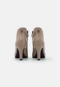 Stivaletti alla caviglia in pelle beige con un design elegante, tacchi alti sottili, cerniere posteriori e dettagli a bottone circolare sulla parte superiore. Texture liscia.
