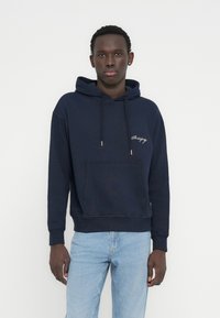 Φούτερ με κουκούλα σε ναυτικό μπλε χρώμα, κατασκευασμένο από μείγμα βαμβακιού, με μπροστινή τσέπη, κουκούλα με κορδόνι, κεντημένο λογότυπο στο στήθος και ριμπ μανσέτες και τελείωμα.