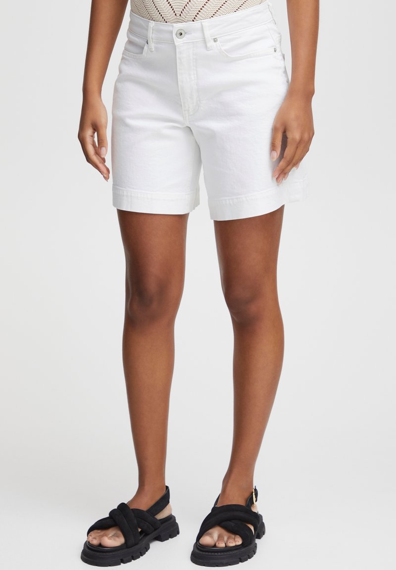 Shorts in denim bianco con taglio dritto, orli risvoltati e chiusura a bottone metallico. Abbinati a sandali neri con cinturini.