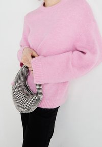 Pink knitted sweater with ribbed cuffs paired with a textured silver rhinestone-patterned handbag. Black pants complete the outfit.