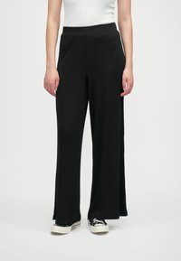 Črne široke hlače iz mehkega materiala z elastičnim pasom. Oblikovanje je prostorno, kar zagotavlja udobje in svobodo gibanja.