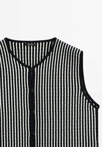 Gilet sans manches en maille à rayures verticales noires et blanches, avec boutons et col rond.