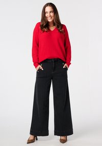 Rood geribbelde trui met een V-hals, gecombineerd met zwarte jeans met wijde pijpen en voorzakken met contrasterende stiksels. Geselecteerd met schoenen met dierenprint.