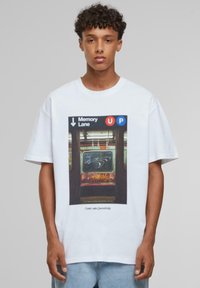 Hvid bomulds t-shirt med et grafisk tryk af en metro-scene, med "Memory Lane" og retningssymboler i blå og røde accenter.